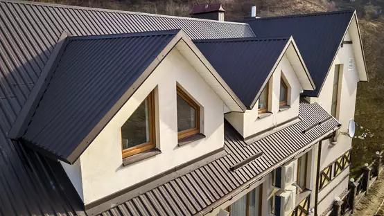 Close-up aerial view of building attic rooms exterior on metal shingle roof, stucco walls and plastic windows.