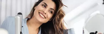 Smiling young lady doing hairstyle while looking at mirror in the room stock photo